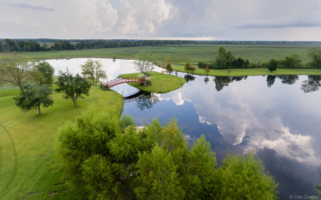 Drone photo of a scenic lake in Sealy, TX. The image captures a bridge, an island, and the sky reflecting on the water's surface.
