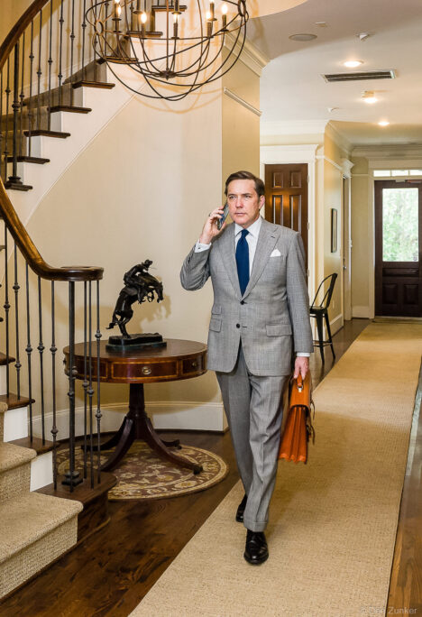 Houston attorney in gray suit carrying leather briefcase and talking on phone in upscale office entryway for law firm branding