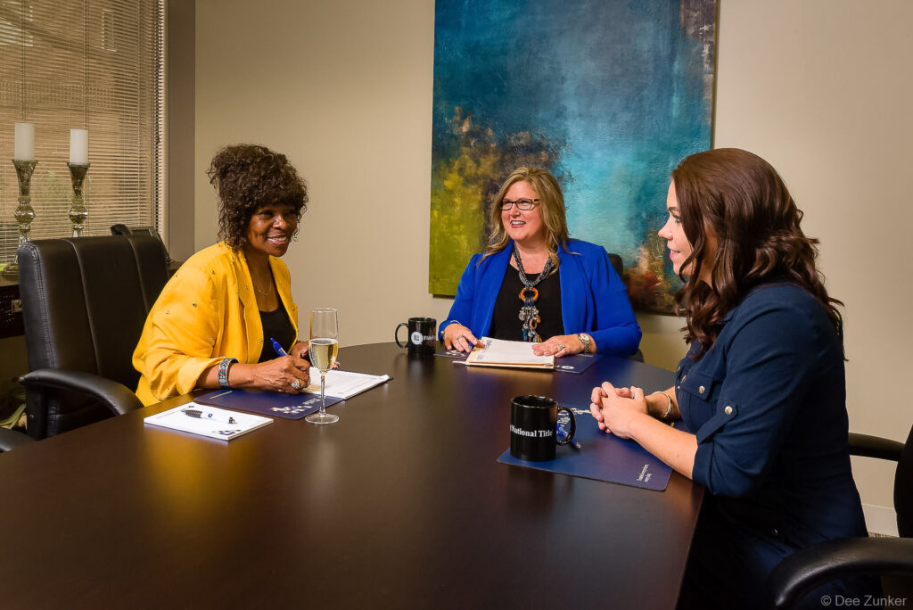 Three professional women discussing documents at a conference table during a financial firm branding lifestyle photo session in Houston