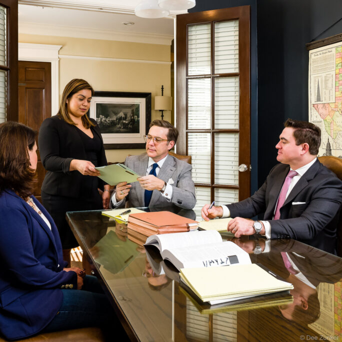 Four legal professionals reviewing documents at a glass conference table in a Houston Heights law firm office