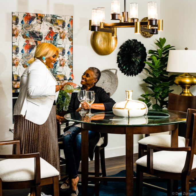 Two women sharing wine at a glass-top dining table in a stylishly decorated Houston interior design showcase room