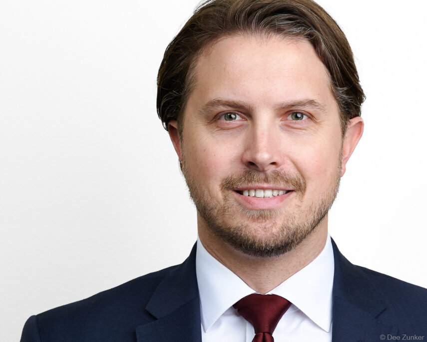 Male attorney in navy suit and red tie poses for a professional corporate headshot against a white studio background in Houston.