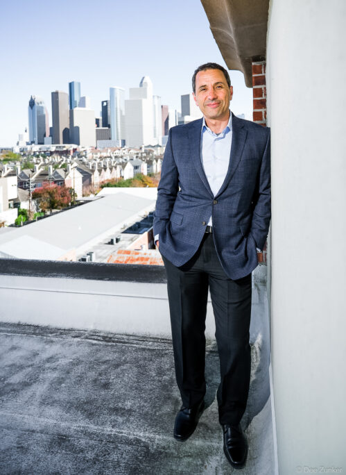 Executive portrait of Precision Roof Crafters company leader in suit on Houston rooftop with downtown skyline backdrop