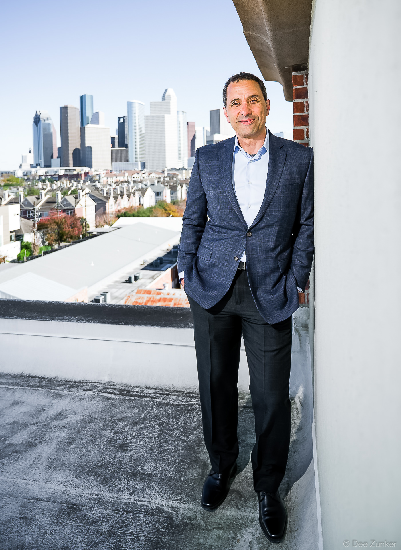 Executive portrait of Precision Roof Crafters company leader in suit on Houston rooftop with downtown skyline backdrop