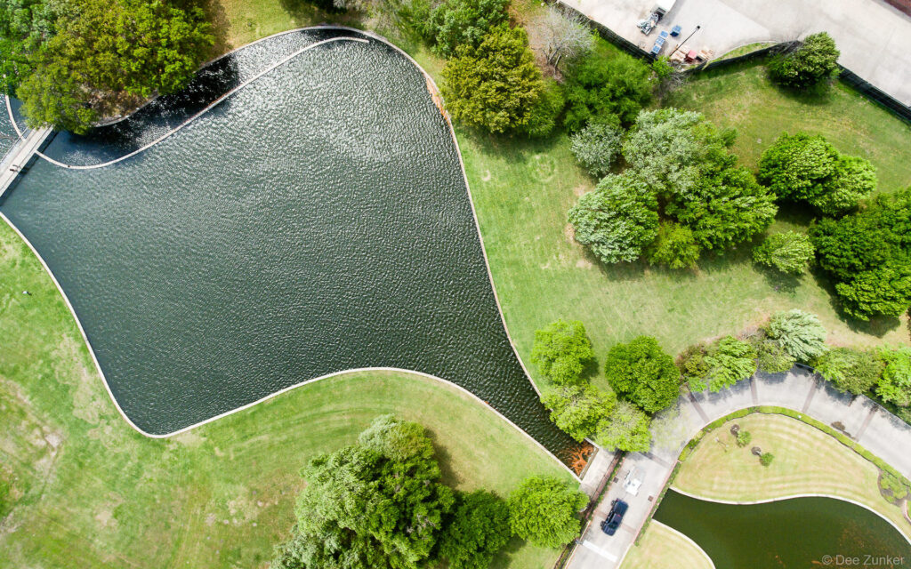 Overhead drone view of Meyer Park in Houston, TX. The aerial shot highlights the lake's interesting shape with ripples from a windy day.