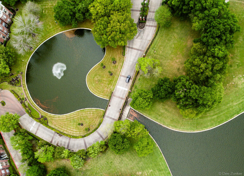 Top-down aerial photo of the lake at Meyerland Park, showing the driveway entrance into a waterfront apartment complex.