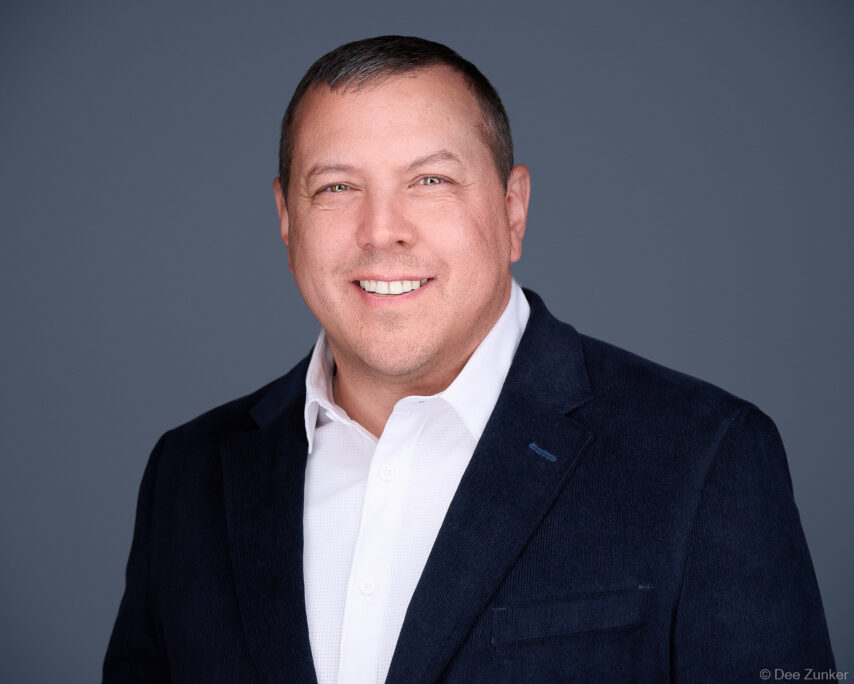 Male oil and gas executive in navy blazer and white shirt poses for corporate studio headshot against gray background in Houston.