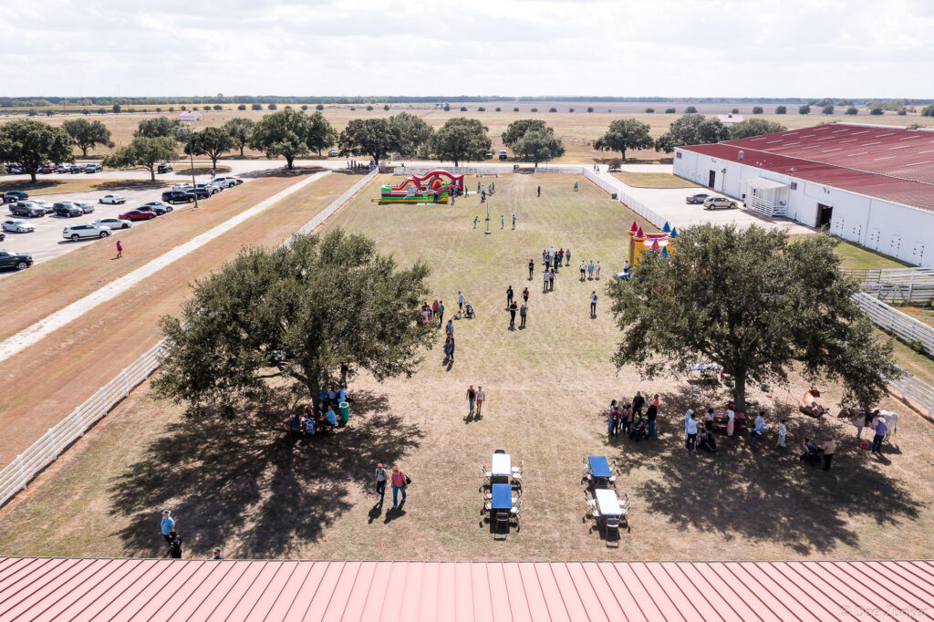 Aerial drone photo of Oceaneering Family Day 2024 outdoor event with bounce houses, picnic tables, and attendees on a Texas ranch property.