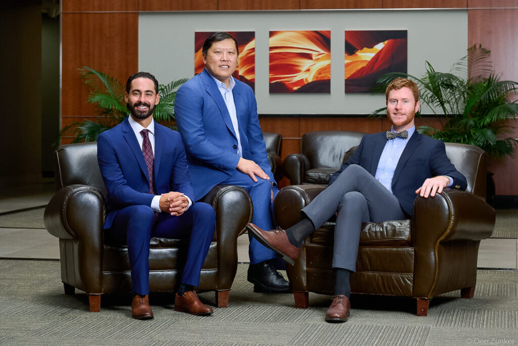 Three professionally dressed male staff members seated in leather chairs for a corporate portrait at OMS in Houston.