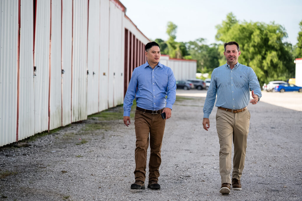 Two business professionals in blue shirts walk along a row of red and white storage units at a Houston commercial property.