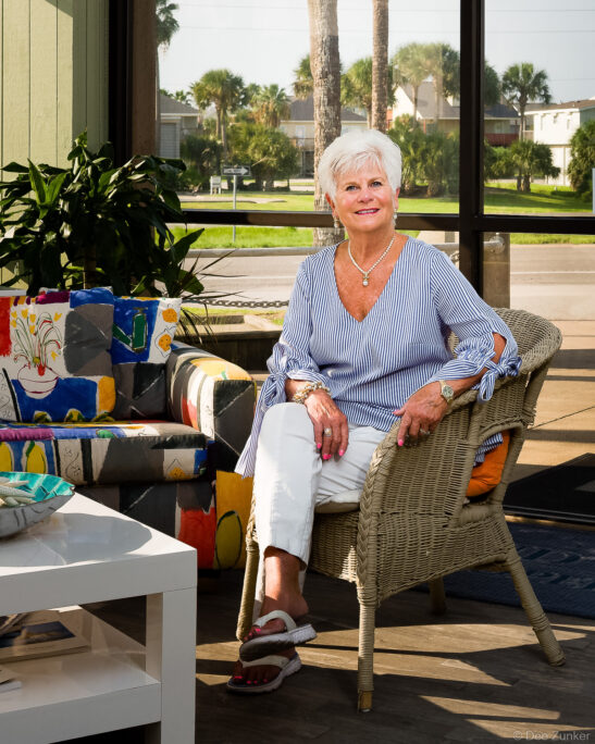 Personal branding portrait of a smiling woman realtor seated in a wicker chair in a bright coastal-style living room, Houston TX