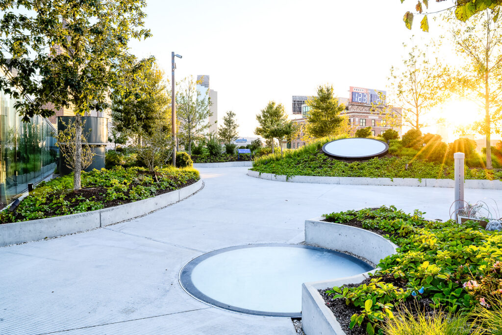 Curved concrete walkways wind through lush rooftop gardens at Post Houston, with downtown skyline visible at golden hour.