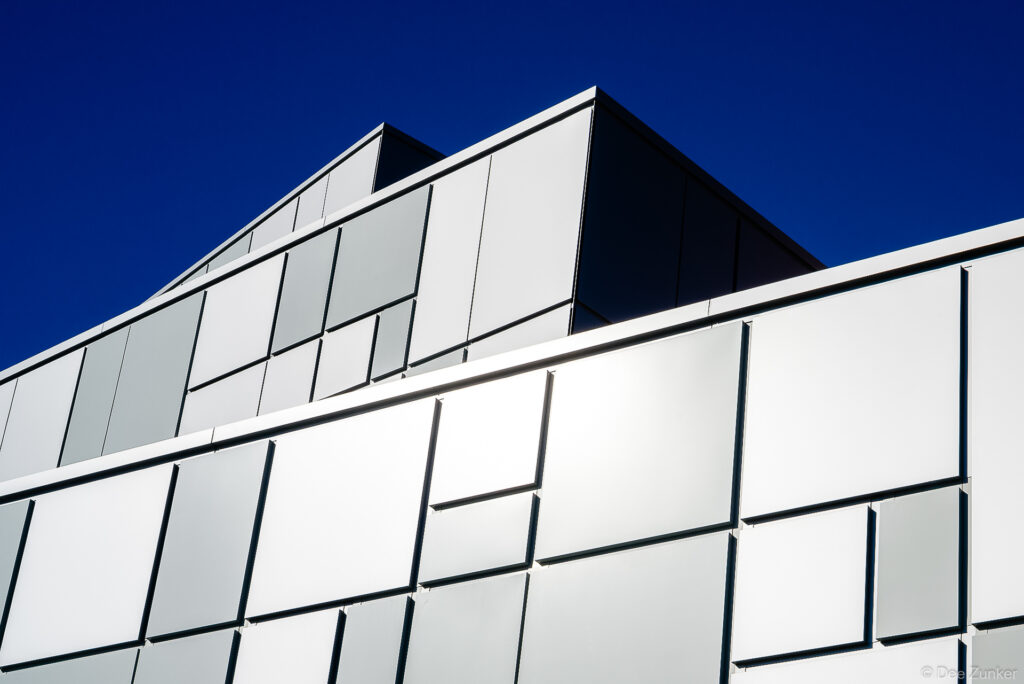 Close-up of a modern building exterior clad in reflective silver metal panels against a deep blue sky, Houston architectural photography.