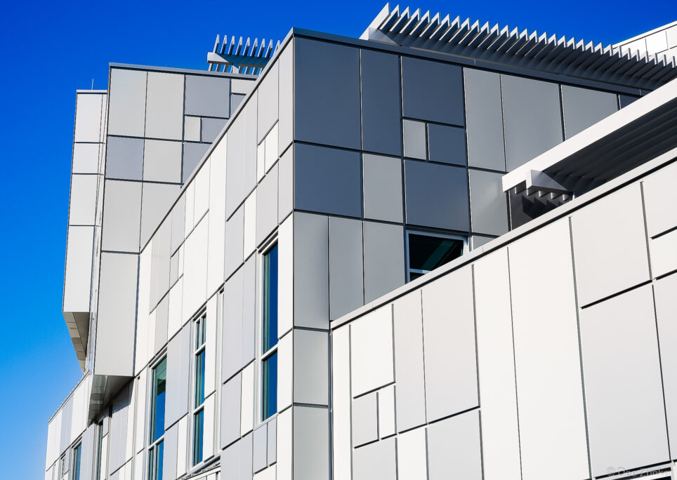 Upward view of a modern Houston commercial building exterior featuring white and dark gray metal cladding panels against a vivid blue sky.