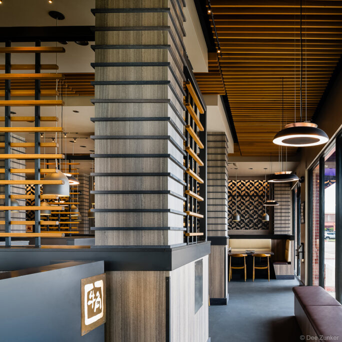 Modern Japanese restaurant interior with wood slat ceiling, pendant lights, geometric wall tile, and booth seating in Houston Texas.