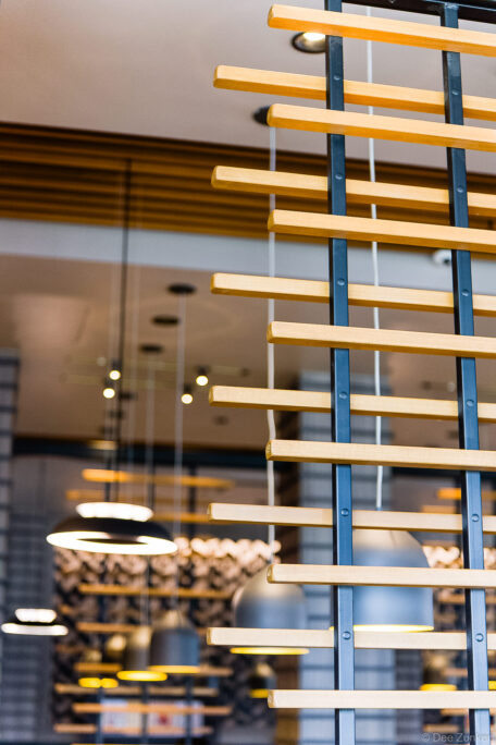 Close-up of wooden slat partition with steel frame in a modern Houston commercial interior, warm pendant lights visible in background.
