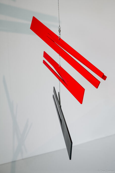 Hanging kinetic art mobile with red acrylic panels and black rectangular elements suspended by wire, Houston product photography studio.