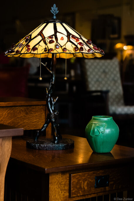 Tiffany-style stained glass lamp with branch base beside a green ceramic vase on a Mission oak side table, Houston product photography.