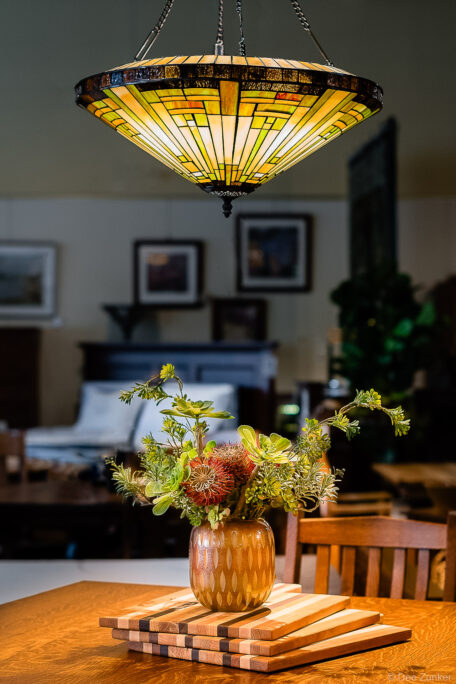 Tiffany-style stained glass pendant lamp above a wood dining table with succulent floral centerpiece, Houston product photography.