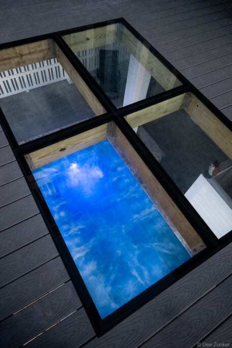 Glass flooring panels set into a gray composite residential deck, revealing a blue illuminated pool below, shot for product portfolio.