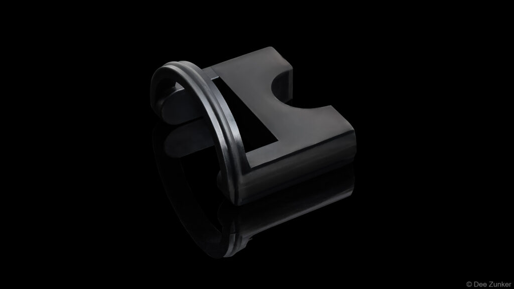 Black anodized industrial drilling tool component with O-ring seal, shot on reflective black background, Houston product photography.
