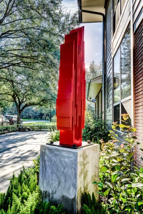 Bold red geometric sculpture mounted on concrete pedestal outside Houston building, captured in professional product photography by Dee Zunker.