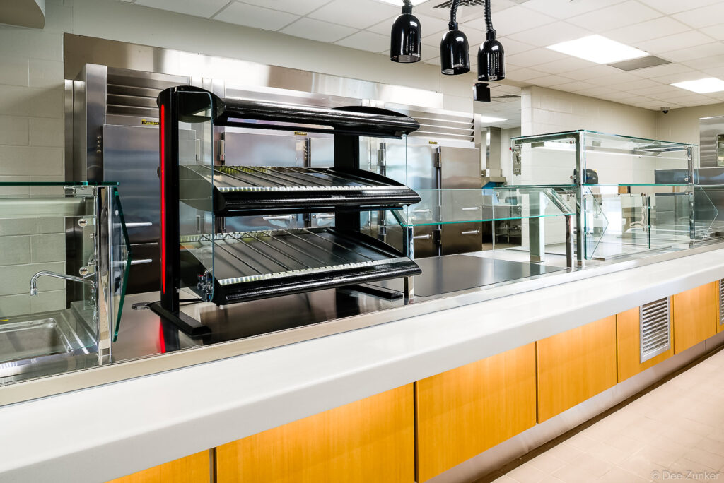 Commercial cafeteria serving line with heated display shelves, sneeze guards, and heat lamps photographed for institutional food service product portfolio.