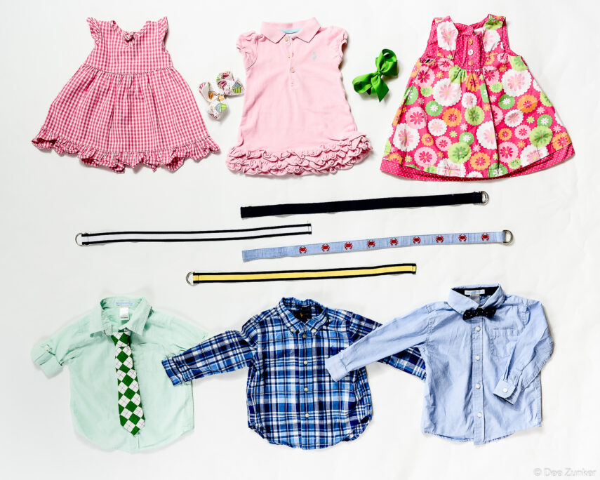 Flat lay product photography of children's dresses, button-down shirts, belts, and accessories arranged on white background, Houston TX.