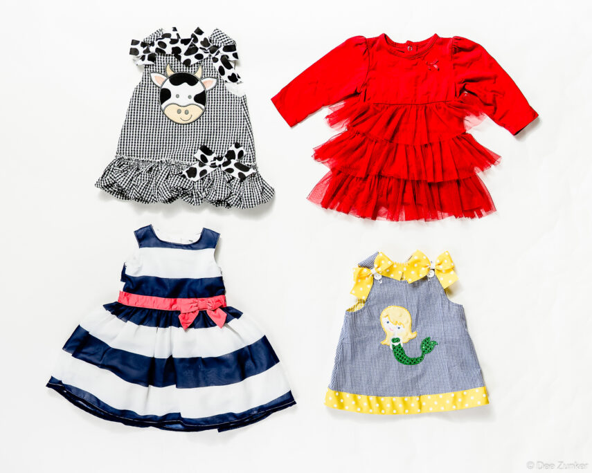 Flat lay product photography of four children's dresses including cow applique, red tulle, navy stripe, and mermaid designs.