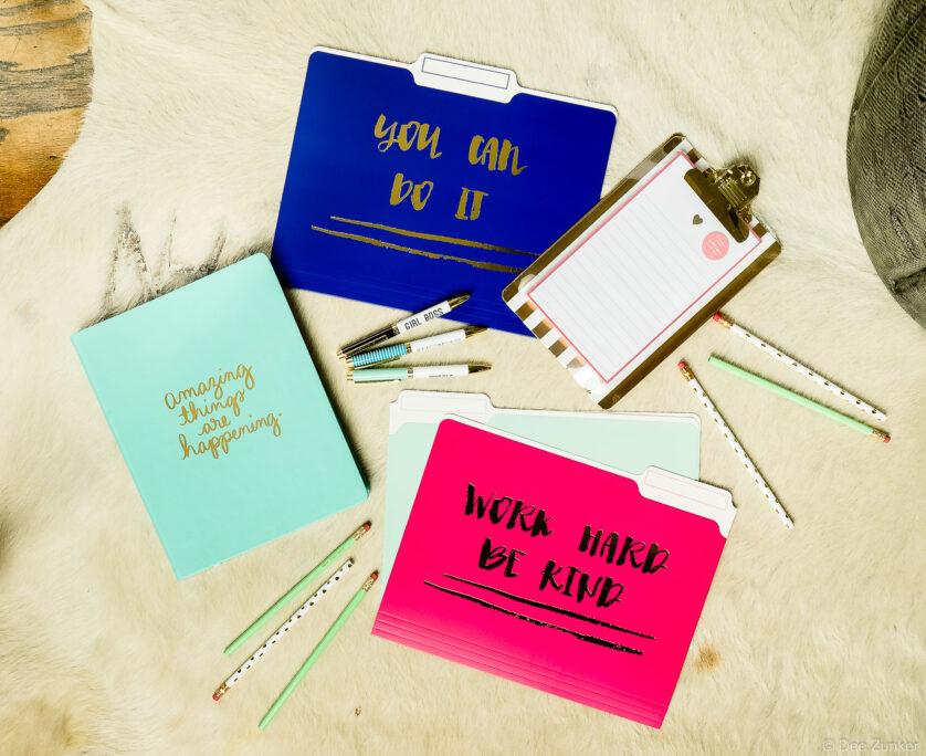 Flat lay product photo of motivational file folders, mint notebook, clipboard, pens, and pencils on white fur surface.