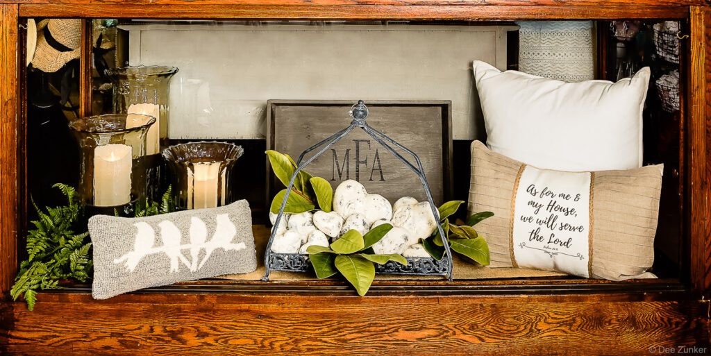 Styled retail vignette featuring decorative pillows, candles, magnolia leaves, and monogram sign photographed for Houston product portfolio.