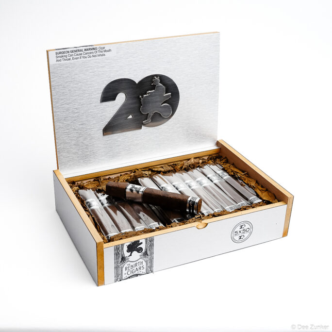 Open luxury cigar box with 20th anniversary branding displaying wrapped cigars on tobacco leaves, shot on white background for retail product photography.