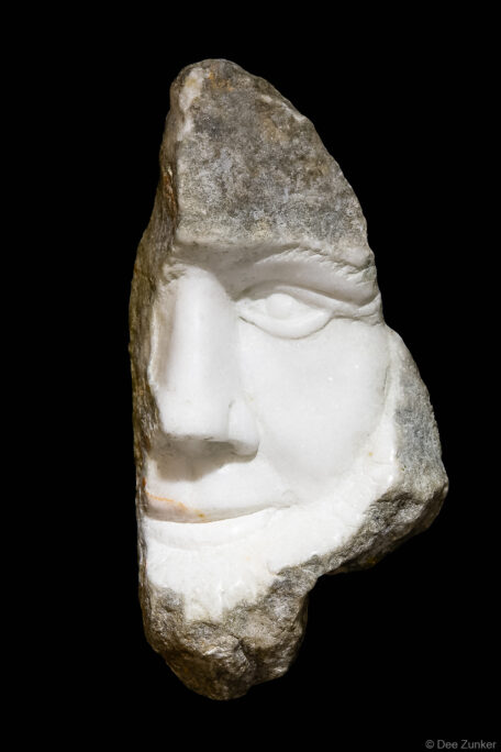 Fragment of white marble sculpture revealing a carved human face emerging from rough stone, Houston product photography by Dee Zunker.