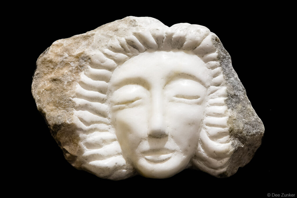 Polished white marble face sculpture with radiating carved rays emerging from rough stone, Houston product photography by Dee Zunker.