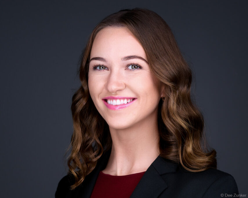 Woman attorney or consultant smiles in studio corporate headshot, gray background, dark blazer, shot by Houston commercial photographer.