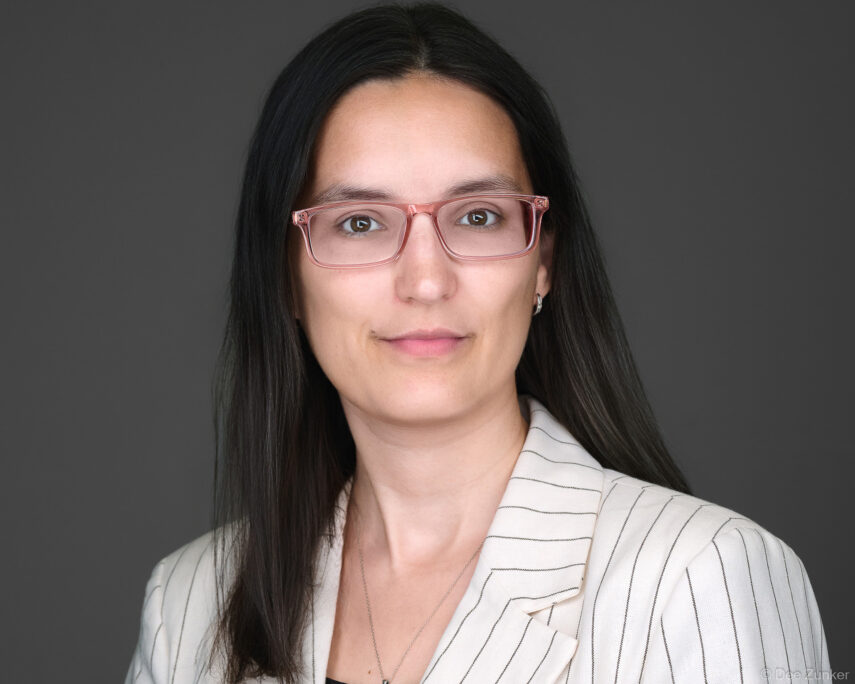 Woman attorney or professional in pink glasses and striped blazer poses for a studio corporate headshot against a gray background in Houston.