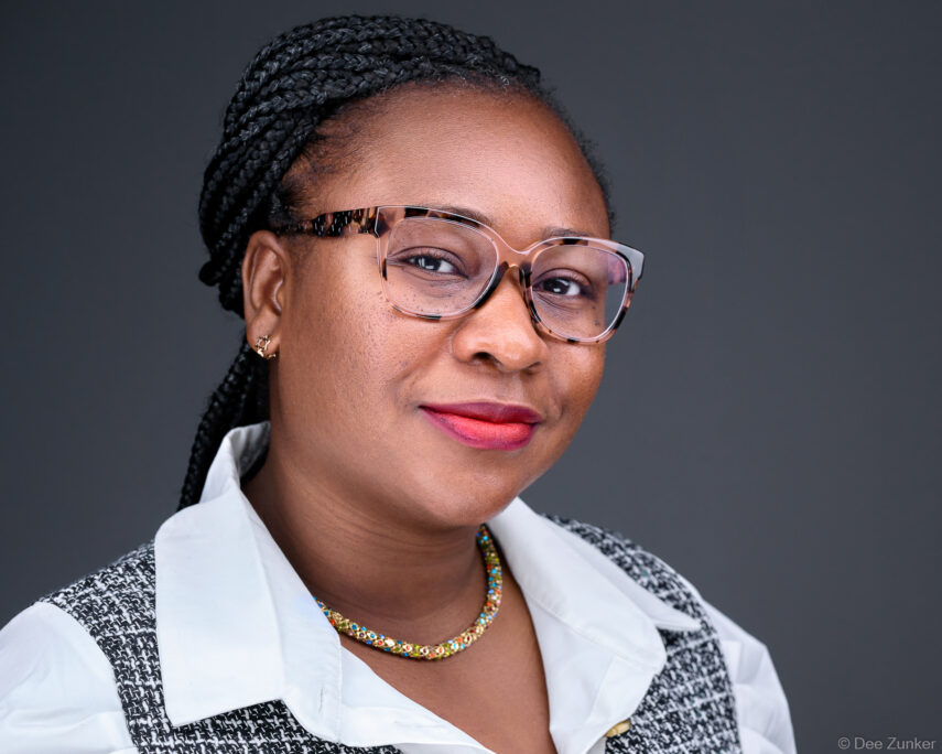 Professional woman in pink glasses and braids poses for corporate headshot against gray studio background in Houston