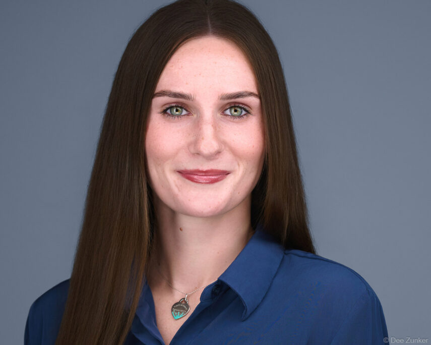 Female attorney with long brown hair and green eyes poses for a professional studio headshot against a gray background in Houston.
