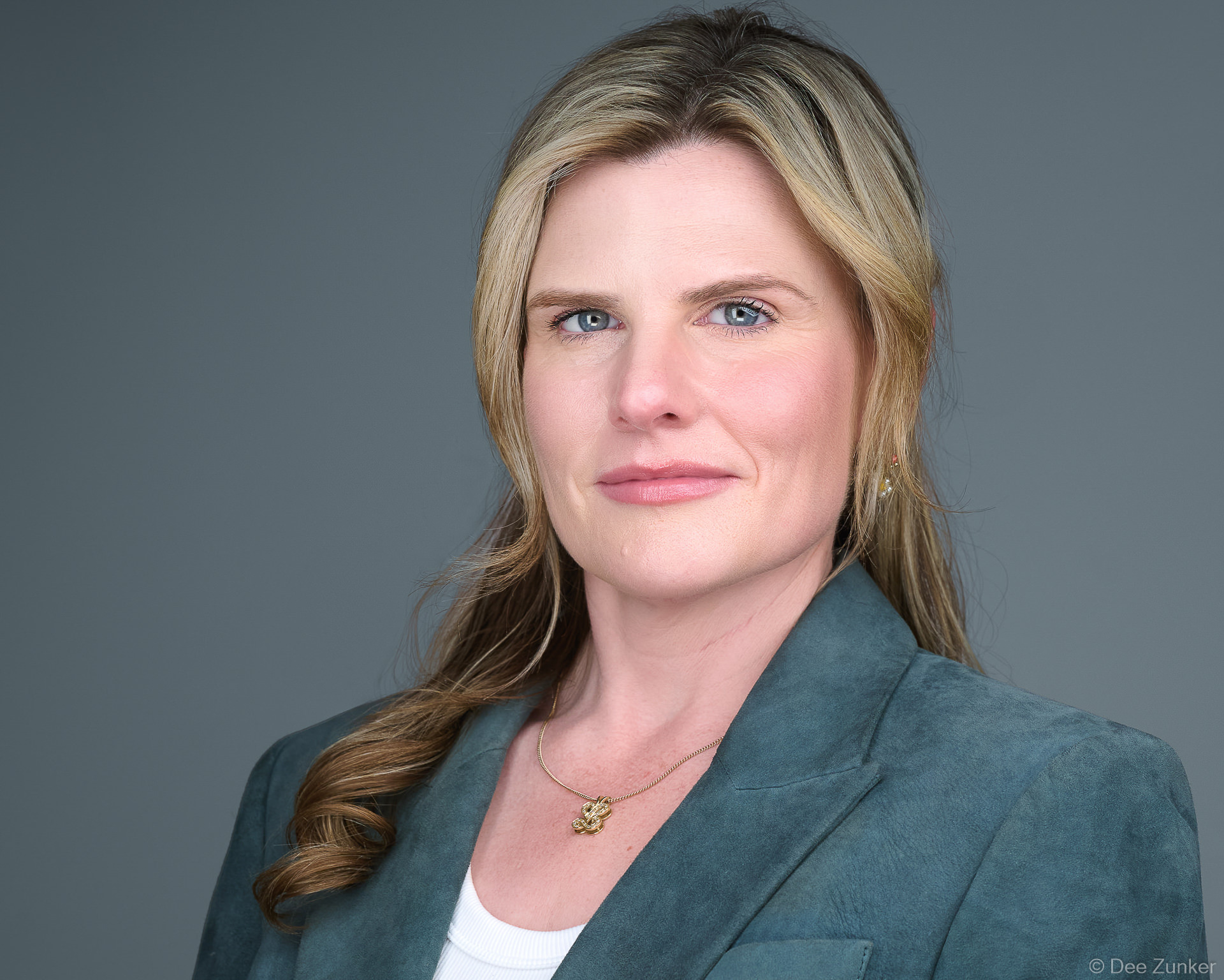 Woman in teal suede blazer poses for a serious professional corporate headshot against a gray studio background in Houston.