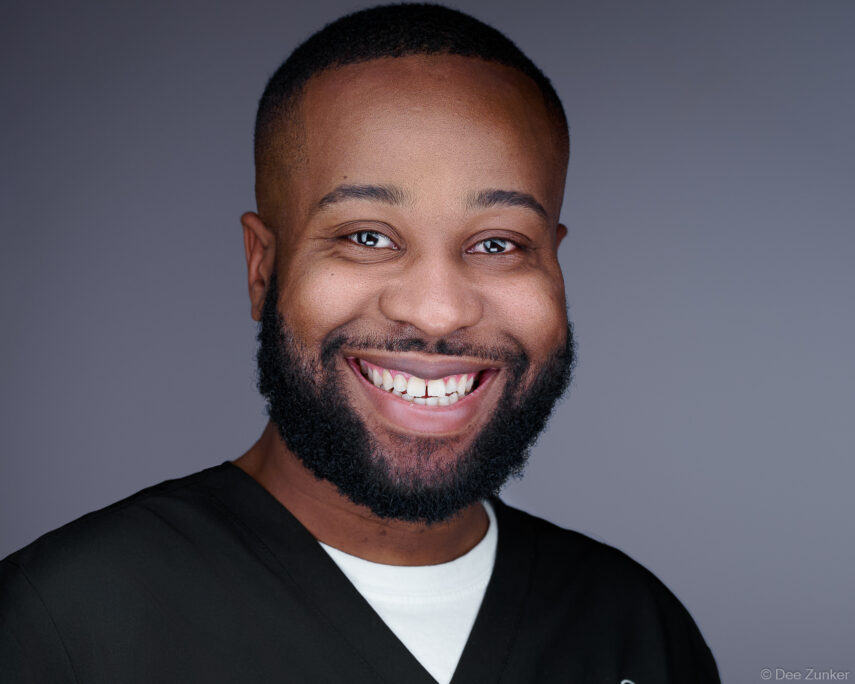 Male healthcare professional smiling in black scrubs against gray studio background, corporate headshot by Houston photographer.