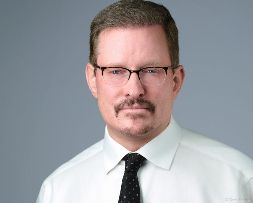 Male attorney or executive in white shirt and dark tie poses for a studio corporate headshot against a gray background in Houston.