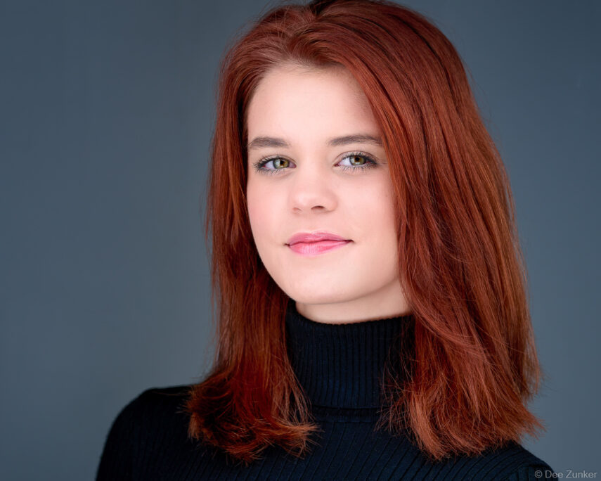 Professional corporate headshot of a redheaded woman attorney in a black turtleneck against a gray studio background, Houston TX.