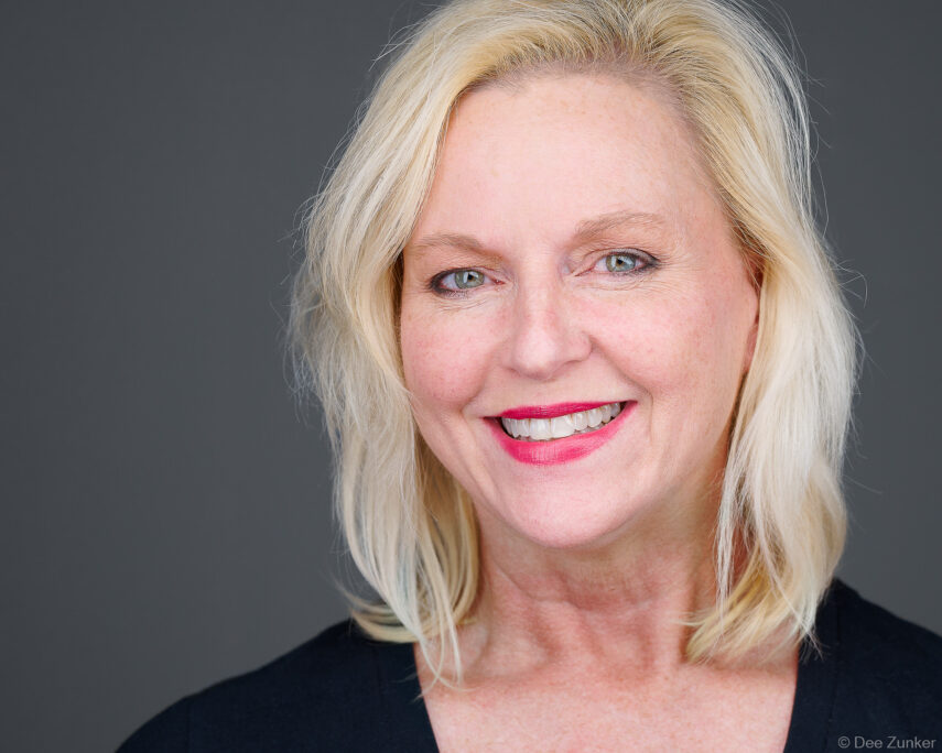 Blonde woman smiles in professional studio headshot against gray background, corporate portrait by Houston commercial photographer Dee Zunker.