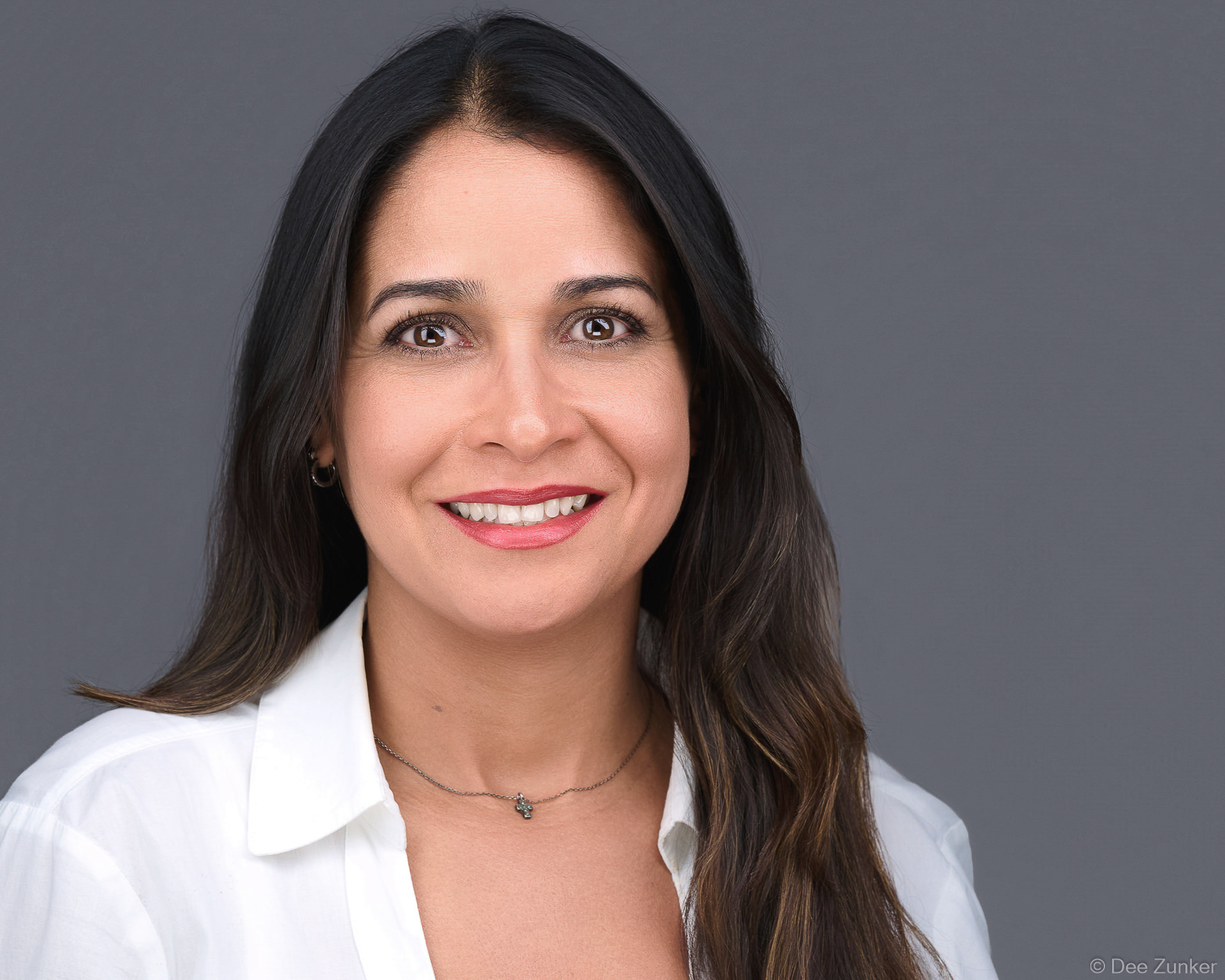 Professional woman smiling confidently in a white blouse against a gray backdrop, studio-lit corporate headshot, Bellaire Houston TX.
