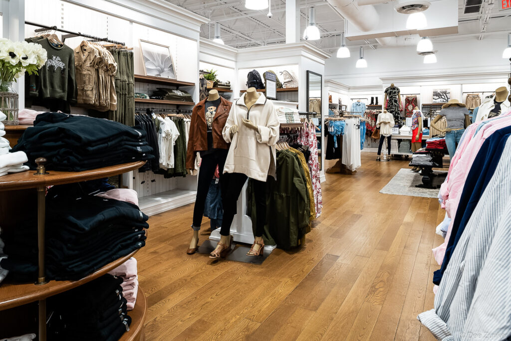 Bright women's clothing boutique interior at RL Cypress featuring mannequins, folded apparel displays, and warm hardwood floors.