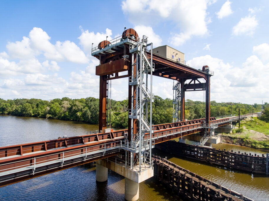 Aerial view of San Bernard River vertical lift railroad bridge, rust-patinated steel tower with machinery, Houston Texas region.
