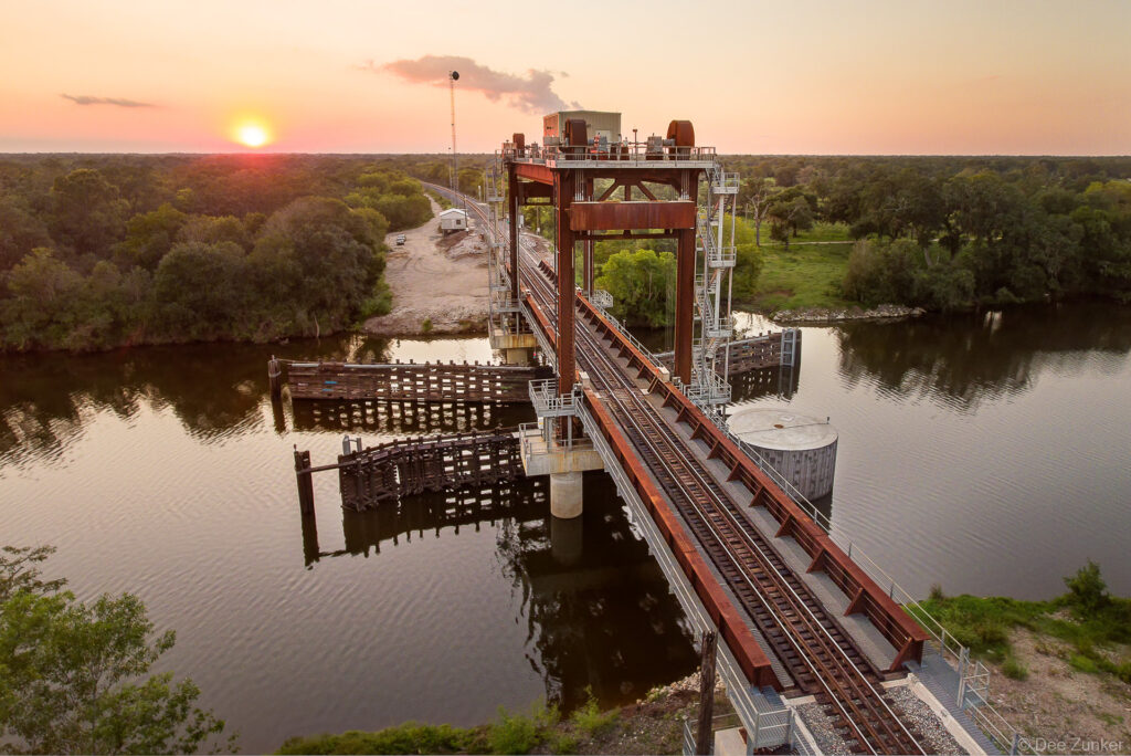 Aerial drone view of the San Bernard River vertical-lift train bridge at sunset, highlighting the industrial infrastructure.