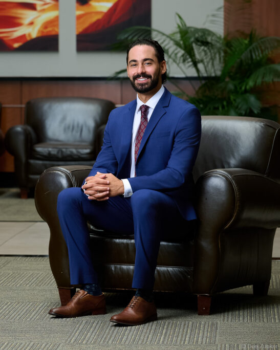 Male professional in navy suit seated in leather chair, corporate staff portrait for OMS, Houston TX.