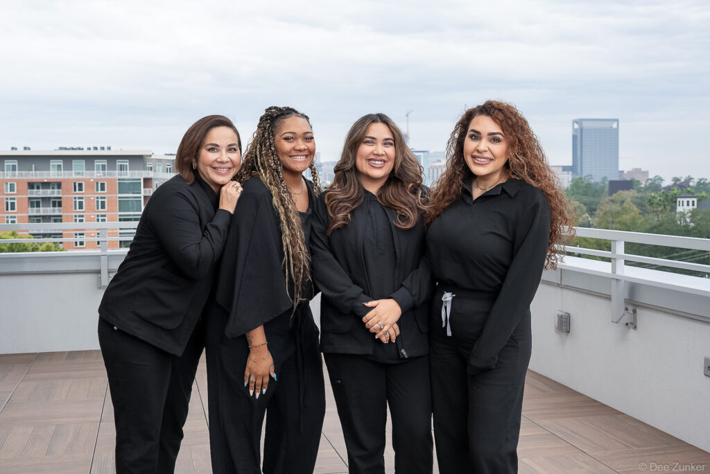 Four smiling women in black uniforms pose on a rooftop terrace at Surgery Center in Houston's Binz district.