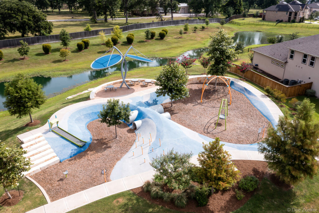 Aerial drone view of Clements Crossing community playground with splash pad, climbing structures, and pond, Houston TX.